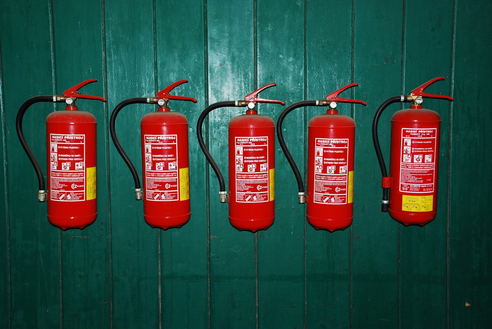 four fire extinguishers lined up against a green wall